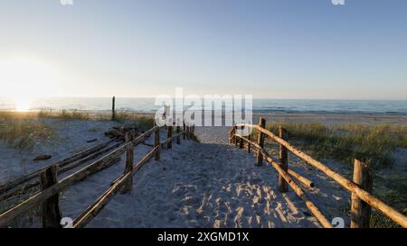 Entrée de sable à la plage. Coucher de soleil. Balustrades en bois. Empreintes de pas dans le sable. Dunes couvertes d'herbe. Slajszewo, Pologne. Mer Baltique Banque D'Images