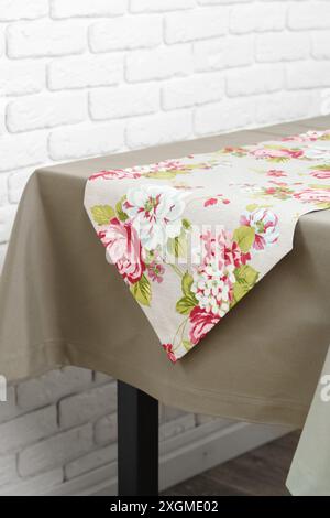 Chemin de table floral sur une nappe beige contre un mur de briques blanches Banque D'Images