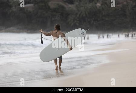 Un surfeur avec sa planche de surf marchant sur la plage de Phuket Thaïlande. Cours de surf à Phuket. Cours de surf à Phuket. Juillet 7,2024 Banque D'Images