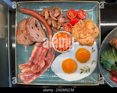 Copieux petit déjeuner avec bacon, œufs frits, saucisses, pain de grains entiers, champignons, tomates, pommes de terre sautées et haricots cuits au four. Un début de journée appétissant et nutritif. Banque D'Images