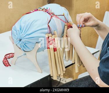 Les mains féminines tournent la sangle sur les bobines. Technique spéciale de tissage de dentelle, motif créé à l'aide d'outils spéciaux : rouleau et bobines. Les bobines sont spéciales w Banque D'Images