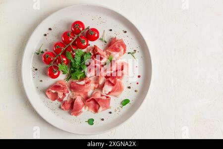 Prosciutto tranché, apéritif, avec tomates cerises, sur une assiette blanche, vue de dessus Banque D'Images