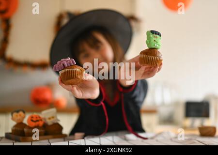 Fille mignonne dans des costumes de sorcière tenant de délicieux cupcakes d'Halloween. Sélectionnez Focus sur la main Banque D'Images