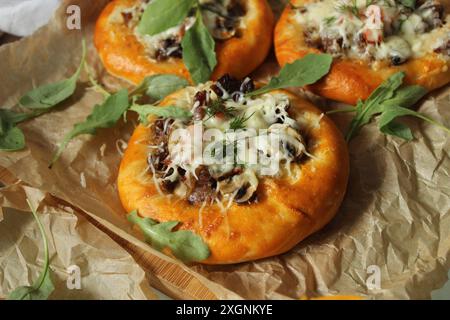 Mini pizzas fraîchement cuites garnies de champignons, fromage fondu, roquette sur papier parchemin Banque D'Images