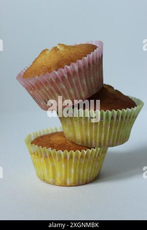 Trois cupcakes empilés dans des gobelets en papier de couleur pastel sur un fond minimaliste Banque D'Images