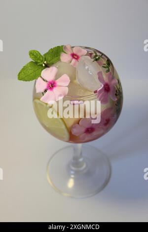 Un cocktail rafraîchissant garni de fleurs roses, de feuilles de menthe et d’une tranche de citron, servi dans un verre avec des glaçons Banque D'Images