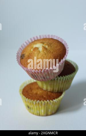 Trois muffins empilés dans des gobelets en papier rose et jaune sur un fond blanc simple Banque D'Images