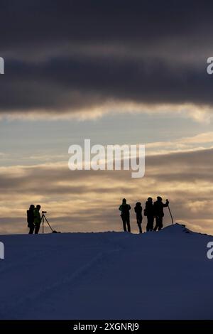 Silhouettes, touristes rétro-éclairés attendant le coucher du soleil sur la montagne Storsteinen, Tromso, Troms og Finnmark, Norvège Banque D'Images