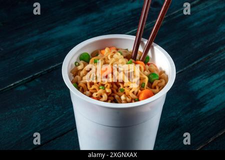 Gobelet de ramen. Nouilles instantanées avec baguettes sur fond en bois bleu foncé Banque D'Images