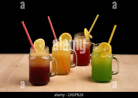 Les boissons colorées dans des pots mason avec des pailles et des tranches de citron sur une table en bois sur fond noir Banque D'Images