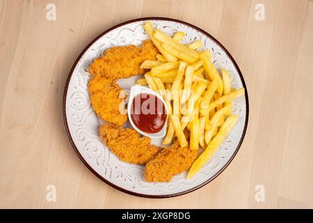 Une assiette d'ailes de poulet frites croustillantes avec des frites et un côté de ketchup sur une table en bois Banque D'Images