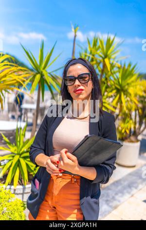 Portrait vertical d'une femme d'affaires prospère dans un complexe de luxe tenant une tablette numérique sous le soleil dans une terrasse Banque D'Images