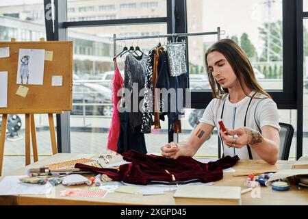 Un jeune homme gay examine attentivement un morceau de tissu dans son atelier de restauration de vêtements, en se concentrant sur la redynamisation des vêtements jetés. Banque D'Images
