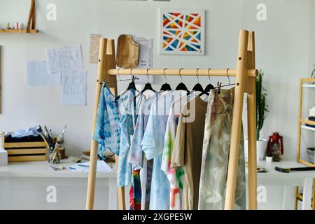 Un porte-vêtements en bois présente une collection de vêtements aux couleurs vives et recyclés dans un studio lumineux. Banque D'Images