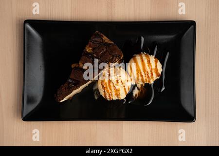 Une vue de dessus d'un délicieux dessert avec une tranche de gâteau au chocolat et deux boules de glace à la vanille dans une assiette noire sur une table en bois Banque D'Images