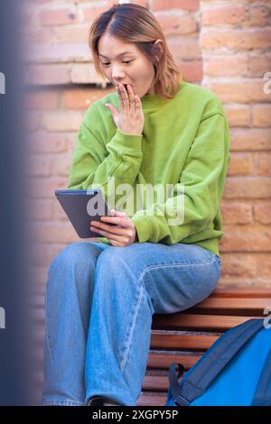 Surprise jeune femme asiatique assise surfant sur Internet sur une tablette numérique. Banque D'Images