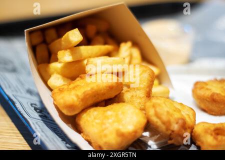 Sur la table, il y a une boîte de nuggets de poulet et de frites. Le repas comprend de la restauration rapide et de la nourriture frite, qui sont des plats de base populaires dans beaucoup Banque D'Images