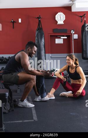 Fit homme afro-américain et jeune femme caucasienne au gymnase, avec espace de copie. Ils partagent un moment de motivation pendant une séance d'entraînement. Banque D'Images