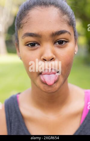 Adolescente biraciale sort sa langue, avec l'espace de copie inchangé. Capturée en extérieur, son expression ludique ajoute une touche de légèreté à la sce Banque D'Images