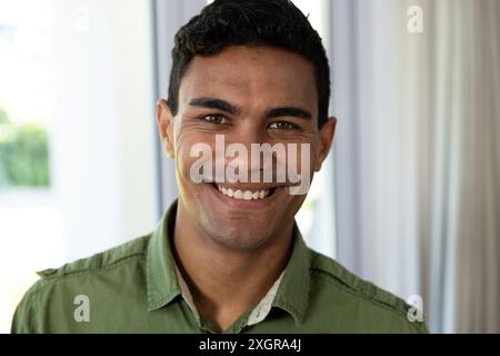 Jeune homme biracial sourit chaleureusement, avec un espace de copie. Son expression joyeuse ajoute une atmosphère accueillante au cadre de la maison inchangée. Banque D'Images