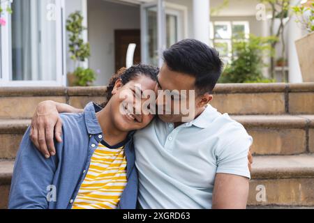 Couple biracial aime une étreinte chaleureuse à l'extérieur, inaltérée. Ils partagent un moment d’affection sur les marches de leur maison. Banque D'Images