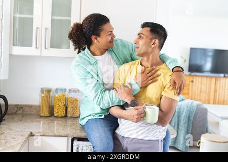 L'homme biracial embrasse son partenaire du moyen-Orient dans une cuisine confortable, avec un espace de copie. Le couple gay partage un moment chaleureux et affectueux à la maison, Radiat Banque D'Images