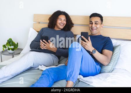 Couple biracial gay aime le temps de loisirs dans la chambre, avec espace de copie. Ils partagent un moment de joie tout en s’engageant avec leur smartphone à la maison. Banque D'Images