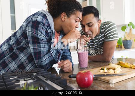 Couple gay biracial et moyen-oriental partagent un smoothie à la maison. Ils profitent d'un mode de vie sain avec une boisson nutritive maison dans la cuisine. Banque D'Images