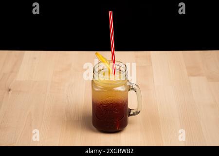 Un pot maçon rempli d'une boisson glacée en couches, garni d'une tranche de citron et d'une paille rayée rouge Banque D'Images