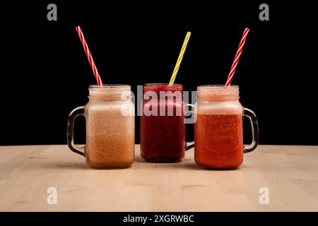 L'arbre mason verres en pot remplis de différents smoothies et pailles sur une table en bois Banque D'Images