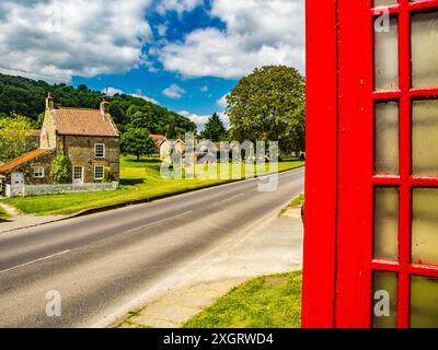 Hutton le Hole, Yorkshire du Nord, Angleterre. regardant de l'autre côté de la route le village vert et beck encadré avec une boîte téléphonique rouge Banque D'Images