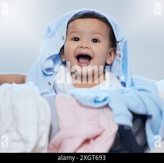 Bébé, enfant et jouer avec la lessive en portrait avec le sourire, apprentissage et développement avec plaisir le matin. Enfant, bébé et excité avec des vêtements, panier Banque D'Images