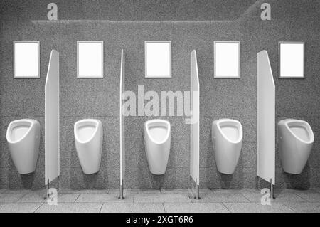 Groupe d'affiches publicitaires blanches vierges accrochées au mur par les urinoirs dans les toilettes pour hommes Banque D'Images