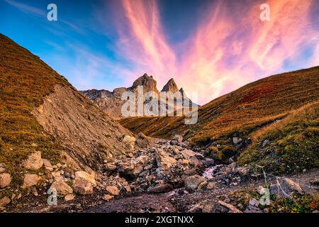 Paysage spectaculaire de ciel de coucher de soleil sur aiguilles d Arves avec trois sommets de montagne rocheux emblématiques et cascade coulant dans la vallée des Alpes françaises à Savoie, Fra Banque D'Images