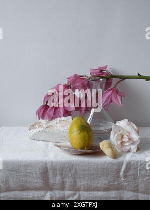 Cette nature morte capture l'atmosphère sereine d'une scène de cuisine avec une miche de pain rustique, une poire mûre, un vase en verre rempli d'orchidées roses Banque D'Images