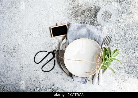 Une table fraîche sur le thème de la menthe pour l'été avec une assiette rustique attachée avec de la ficelle, un brin de menthe, d'élégants couverts et un verre texturé sur un sp Banque D'Images