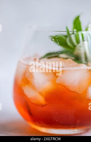 Gros plan d'un cocktail rafraîchissant de Coca-Cola avec de la glace et des feuilles de menthe fraîche dans un verre transparent, avec des gouttelettes d'eau sur la surface réfléchissant la lumière. Banque D'Images