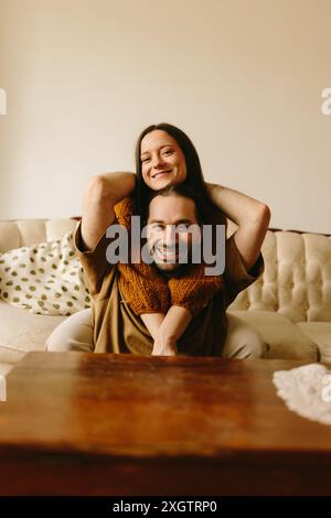 Un couple joyeux profite d'un moment ludique à l'intérieur tandis que la femme est assise sur les épaules de l'homme, les deux souriant largement à la caméra. Banque D'Images