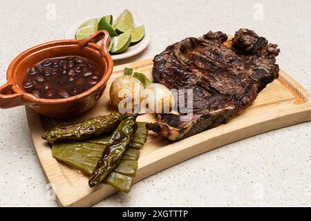 Présentation appétissante de la cuisine mexicaine traditionnelle, avec des côtes grillées sur une planche de bois, accompagnées de piments rôtis, d'oignons et d'un bol de bl Banque D'Images