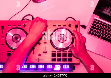 Le DJ ajuste les commandes d'une console de mixage sous des lumières roses intenses, reflétant une ambiance de fête ou de club et montrant la technologie utilisée dans mi Banque D'Images