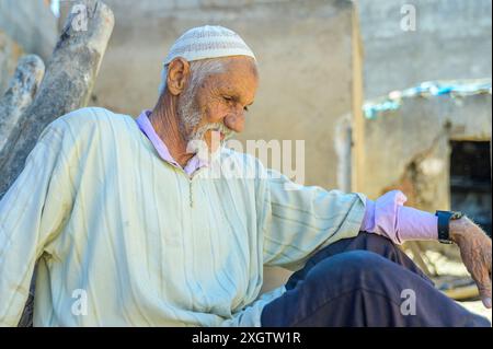 Un marocain âgé porte une djellaba blanche traditionnelle et est assis contemplativement à l'extérieur de sa maison rurale nord-africaine Banque D'Images