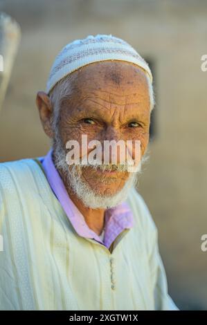 Portrait en gros plan d'un homme marocain âgé portant une casquette blanche traditionnelle et des robes pastel, son visage racontant une histoire à travers des traits profondément lignés Banque D'Images