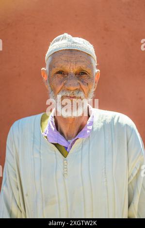 Un portrait d'un homme marocain âgé portant une djellaba blanche traditionnelle et une casquette tricotée il se tient devant un mur aux tons chauds au Maroc, mettant en valeur Banque D'Images