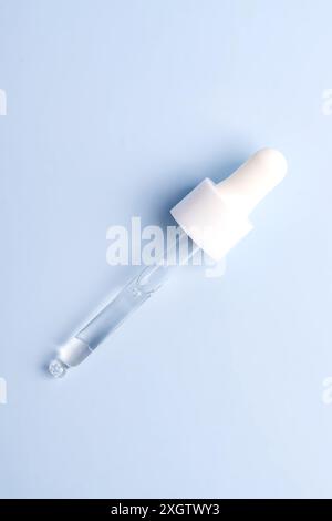 Un compte-gouttes cosmétique transparent rempli de sérum affiché sur un fond bleu doux, mettant l'accent sur la simplicité et la pureté des soins de la peau Banque D'Images
