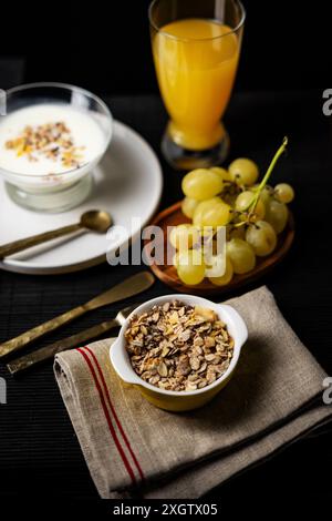 Vue de dessus d'un petit déjeuner nutritif sur un fond sombre, avec un bol de céréales, un verre de jus d'orange et des raisins frais. Banque D'Images