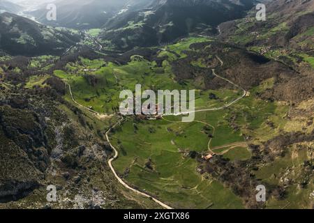 Une photo aérienne capturant un magnifique village de vallée isolé entouré de collines verdoyantes et de routes sinueuses, niché au cœur des terres montagneuses Banque D'Images