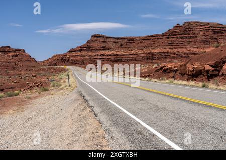 Une route désertique sereine qui traverse le paysage accidenté de White Canyon, qui fait partie de l'aire de loisirs nationale de Glen Canyon, sous un clair bleu Banque D'Images
