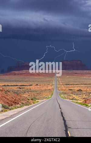 Photo frappante d'un orage éclairant un ciel sombre au-dessus de la route déserte et droite menant à Monument Valley, Arizona Banque D'Images