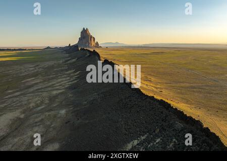 'Une vue aérienne de Shiprock, une formation rocheuse étonnante au lever du soleil dans le vaste désert du Nouveau-Mexique, sous la douce lumière dorée.' Banque D'Images