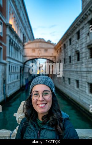 Femme souriante devant le pont historique des Soupirs à Venise, Italie, avec des bâtiments anciens et un canal en arrière-plan Banque D'Images